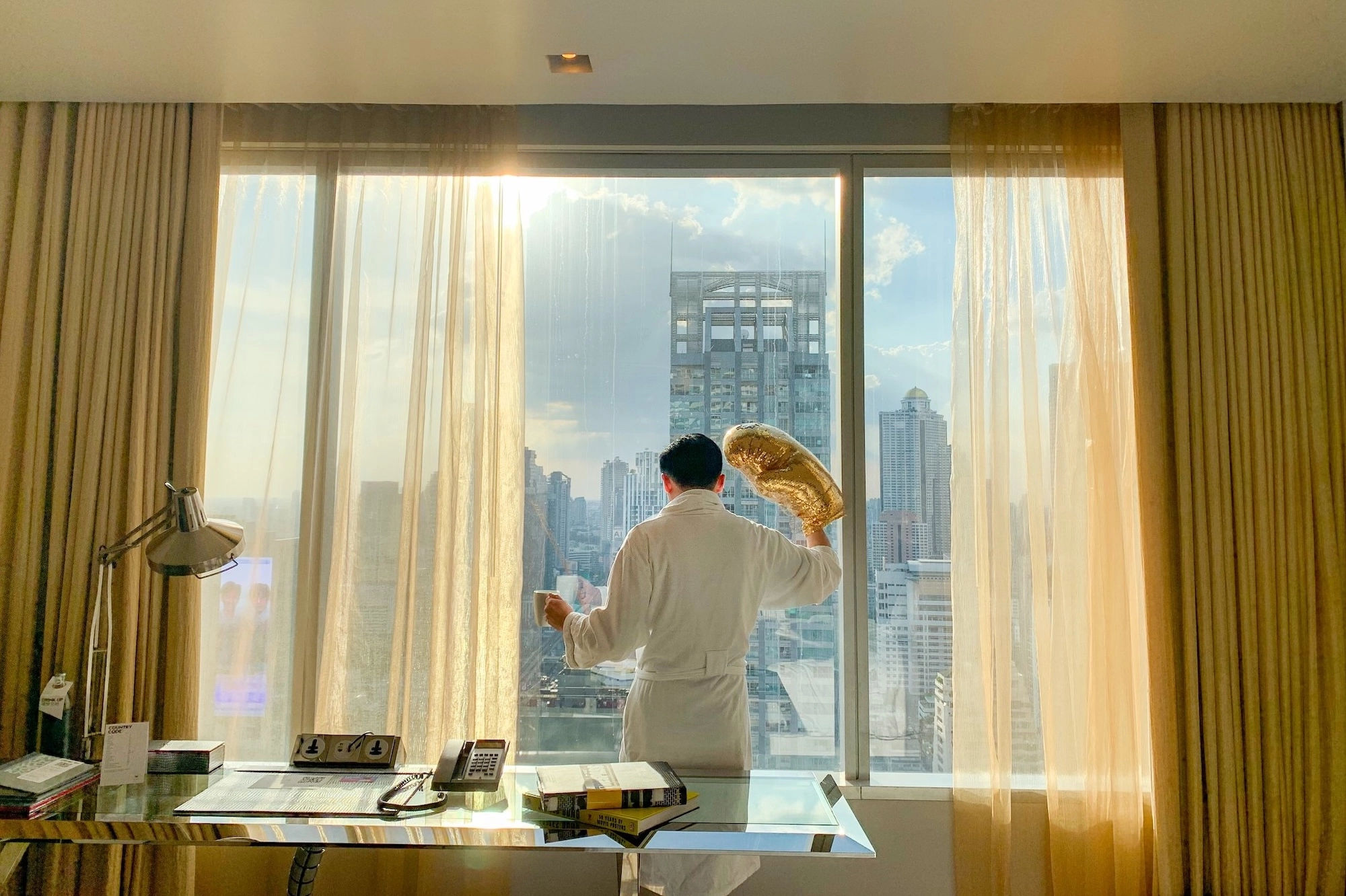 男子在曼谷酒店房间内身穿浴袍佩戴金色手套，呈现奢华放松的氛围