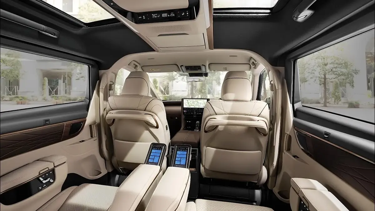 Interior of a luxurious van with beige leather seats, a panoramic sunroof, and individual touchscreens.